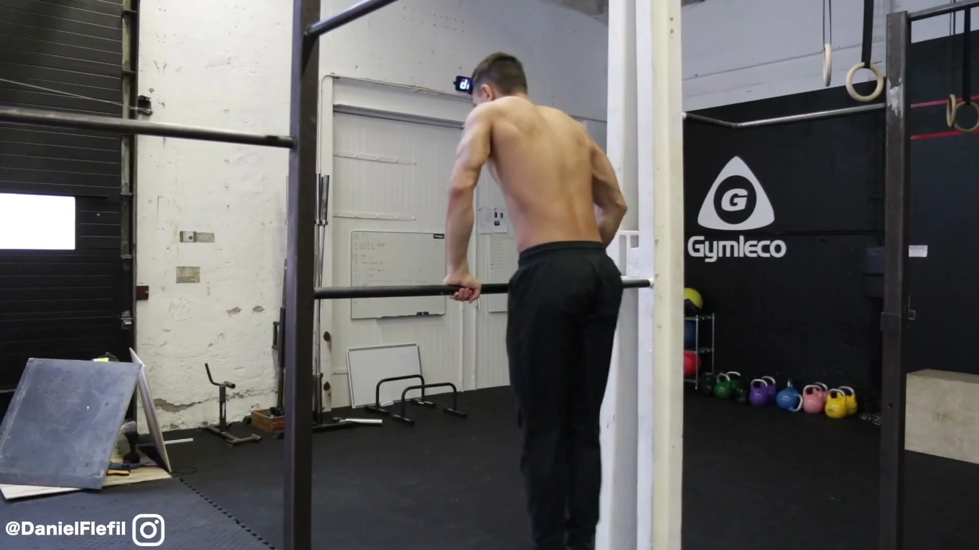 The lean-back trigger for the backward roll on the bar: hips at the bar, upper body beginning to lean backward to start the rotation