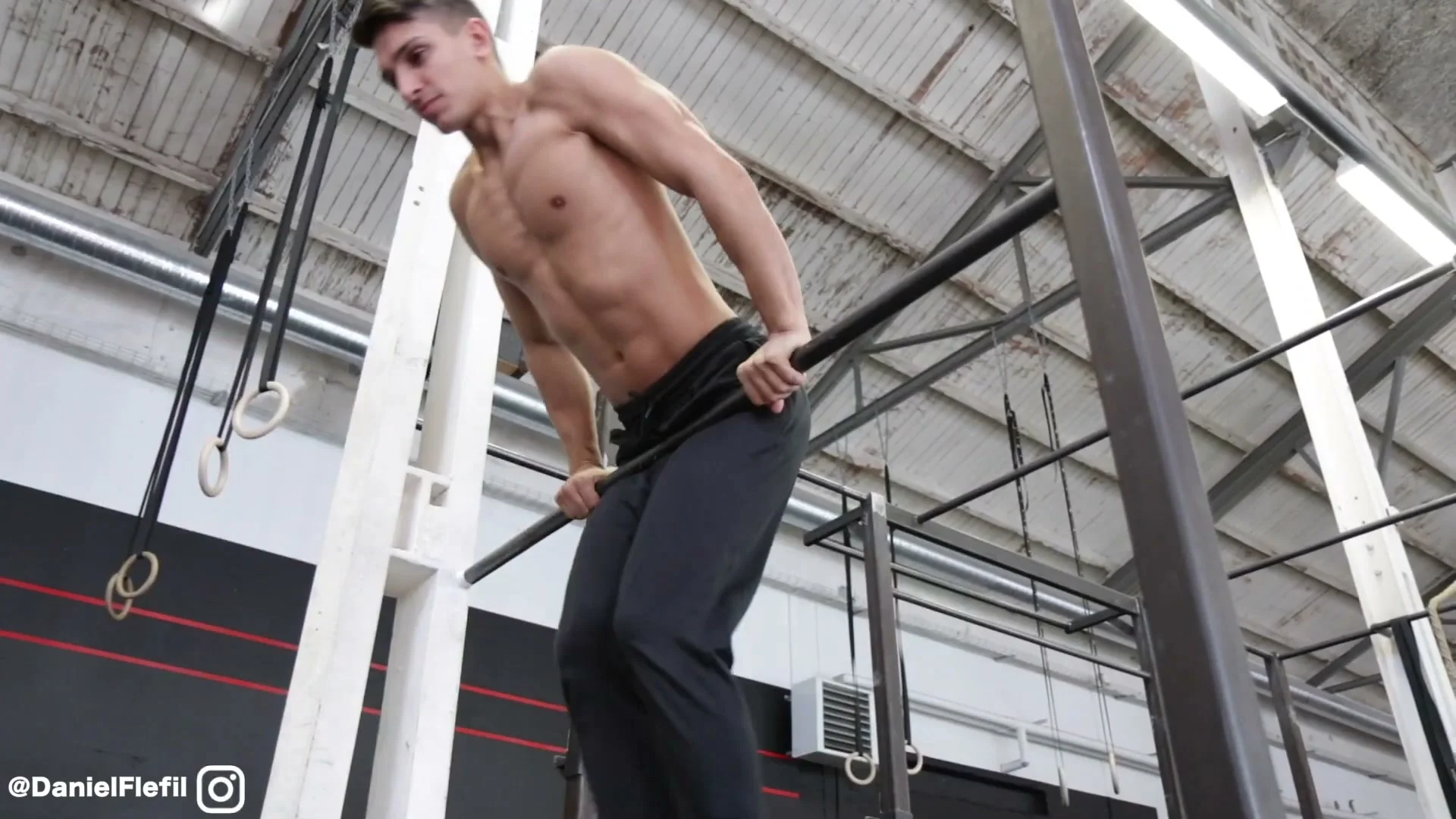 Mid-roll phase of the backward roll on the bar: body rotating backward around the bar, hands gripping through the rotation