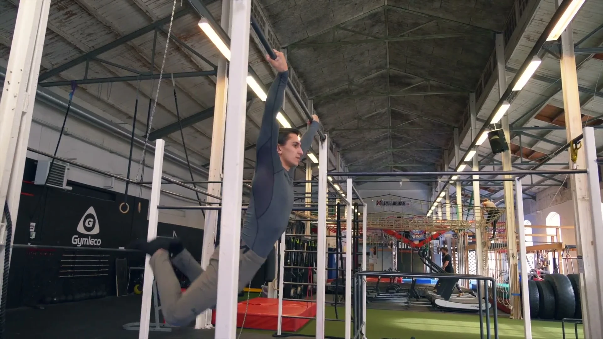 Daniel Flefil swinging on a high bar in the dislocated grip: body extended in the swing with significant height, preparing to release and complete the full 360 spin