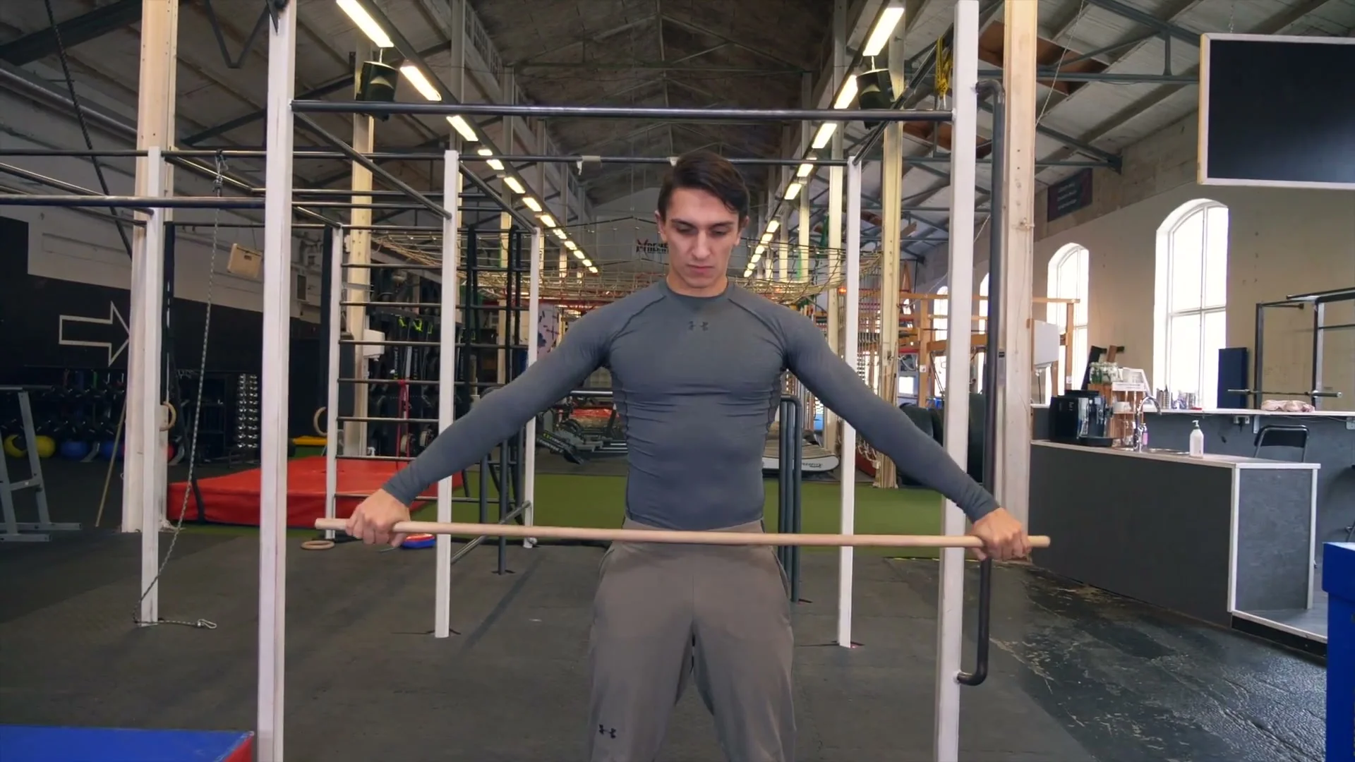 Daniel Flefil demonstrating the stick mobility drill for dislocate 360: holding a wide stick in front of the body, preparing to bring it over the head and behind the back