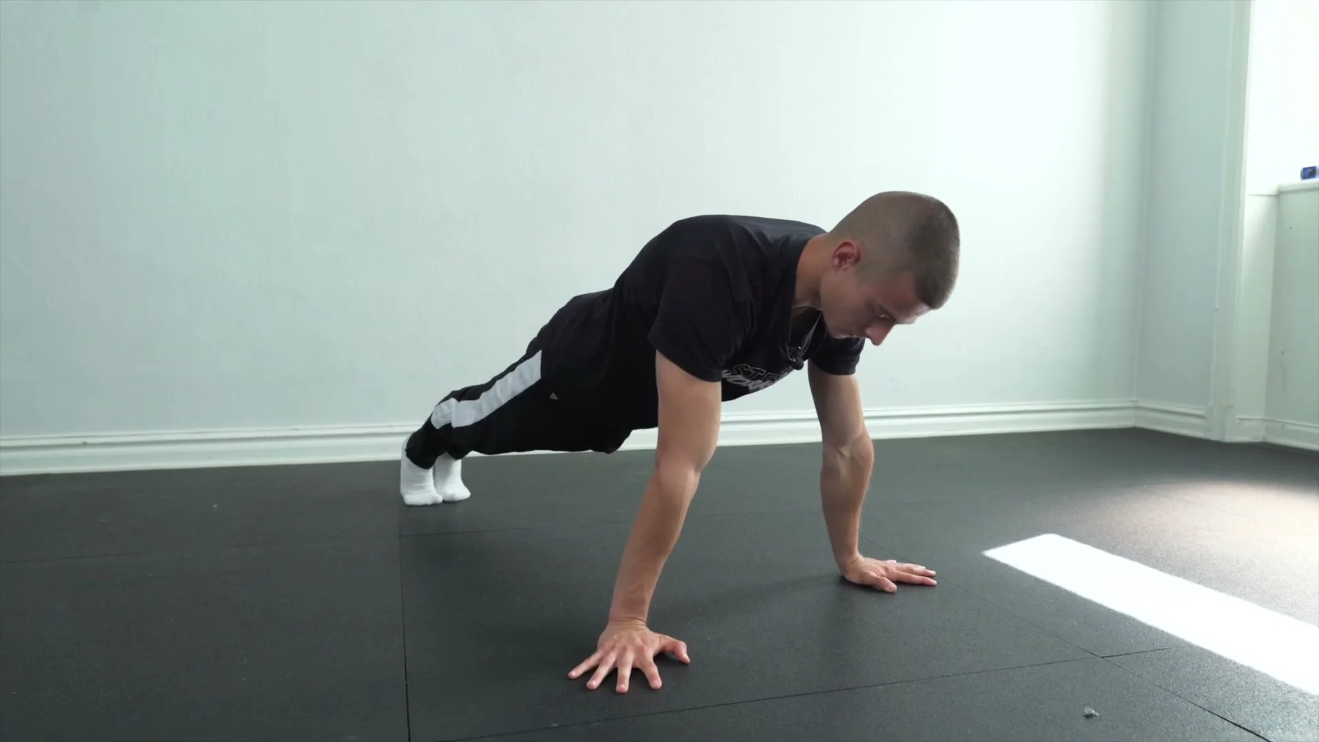 Daniel Hristov in a forward push-up lean position on the floor: body in a straight planche-lean line with elbows and biceps facing forward, demonstrating the standard starting position for explosive planche push-up training