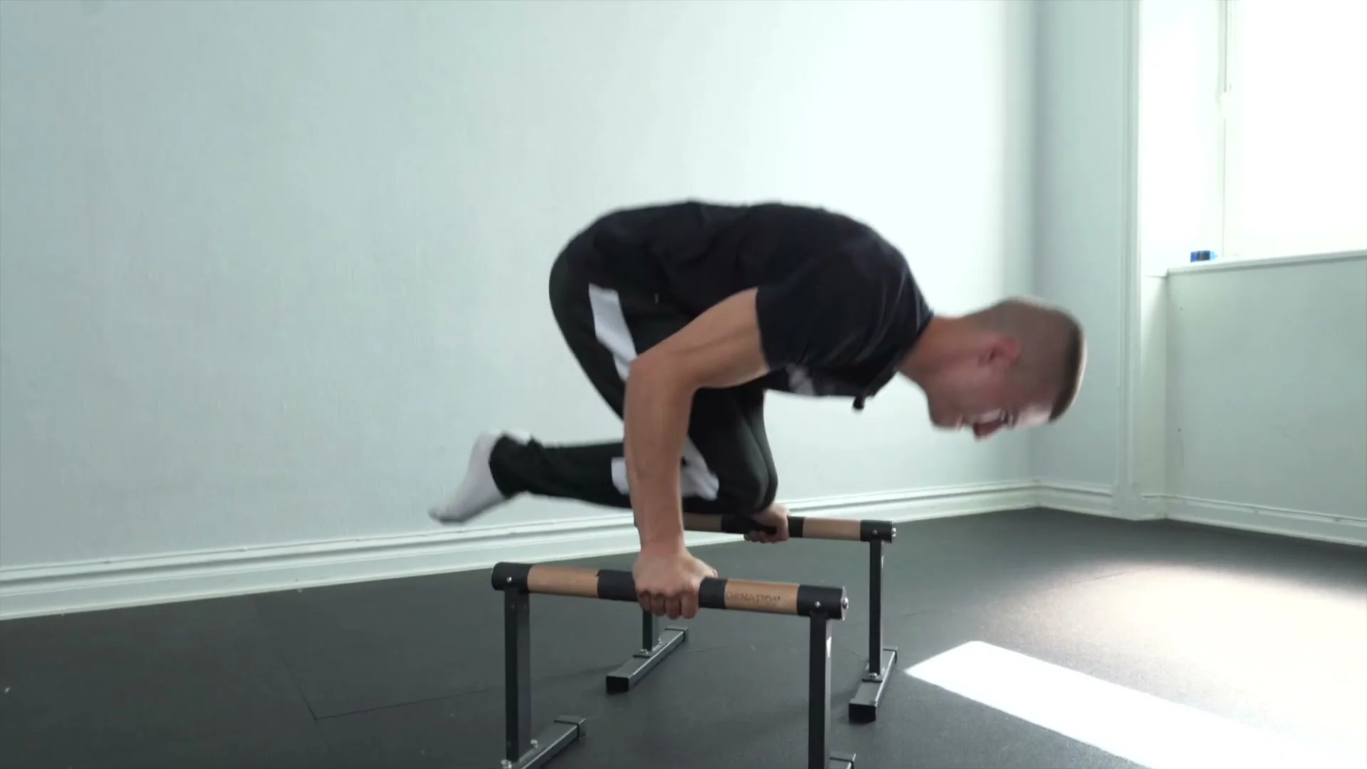 Daniel Hristov performing the push phase of a tuck planche push-up on parallettes: body partially tucked with knees bent and arms bent, demonstrating the explosive push-up from the tuck planche position
