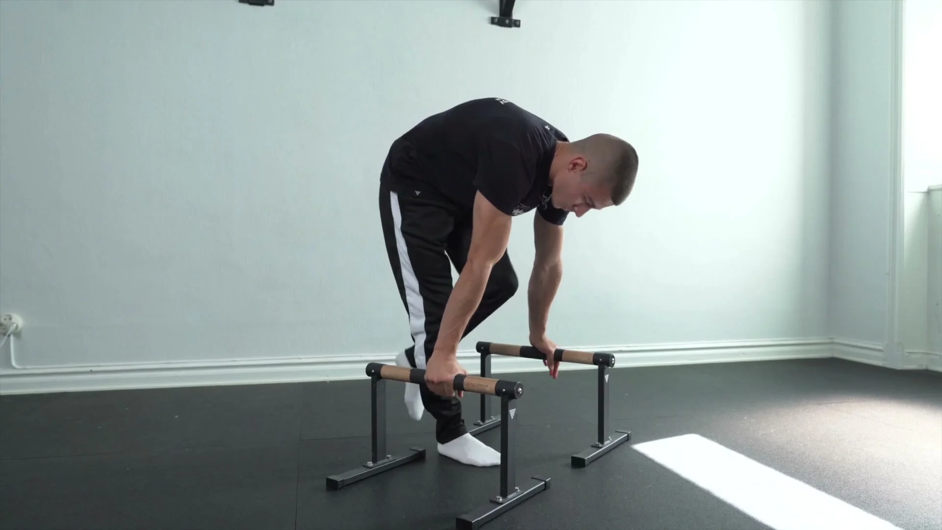 Daniel Hristov setting up on parallettes for the tuck planche push-up: bent over the bars with knees pulled toward the chest, demonstrating the setup position before entering the tuck planche for the third tip