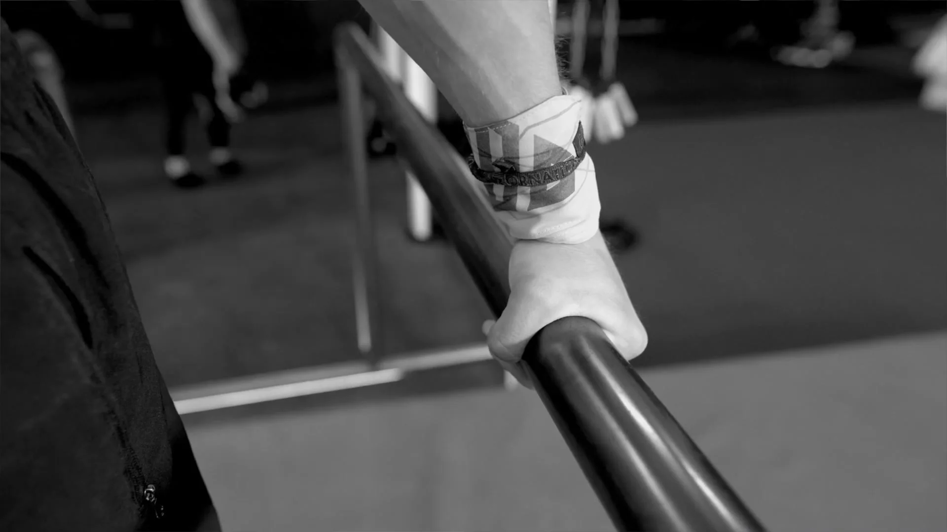Close-up of a hand gripping a P-bar with wrist wraps, showing the correct grip position for the front flip dismount on parallel bars
