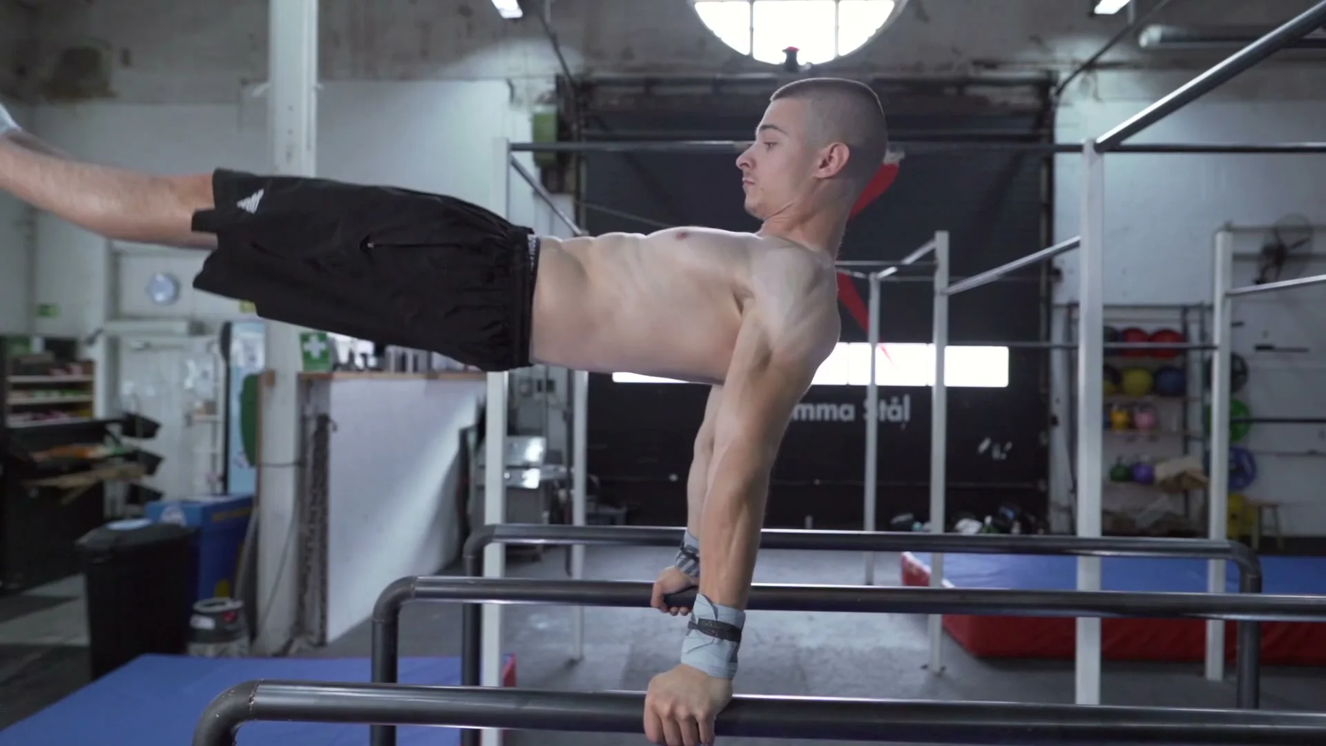 Daniel Hristov with legs extended horizontally on parallel bars in the forward swing position: chest open, body nearly parallel to the ground during the P-bars swing