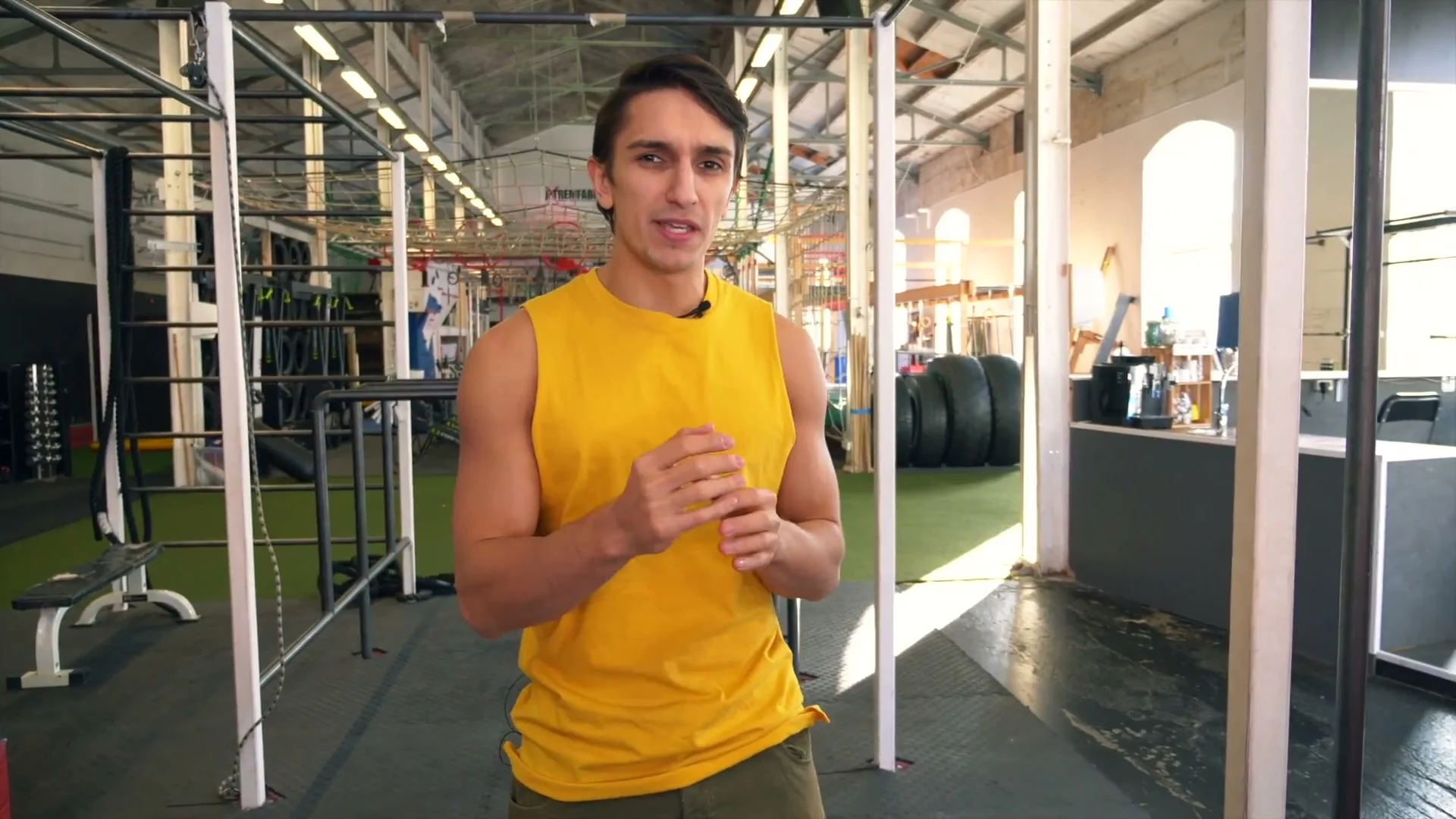 Daniel Flefil explaining the front roll at a gym, yellow tank top, bars visible in background