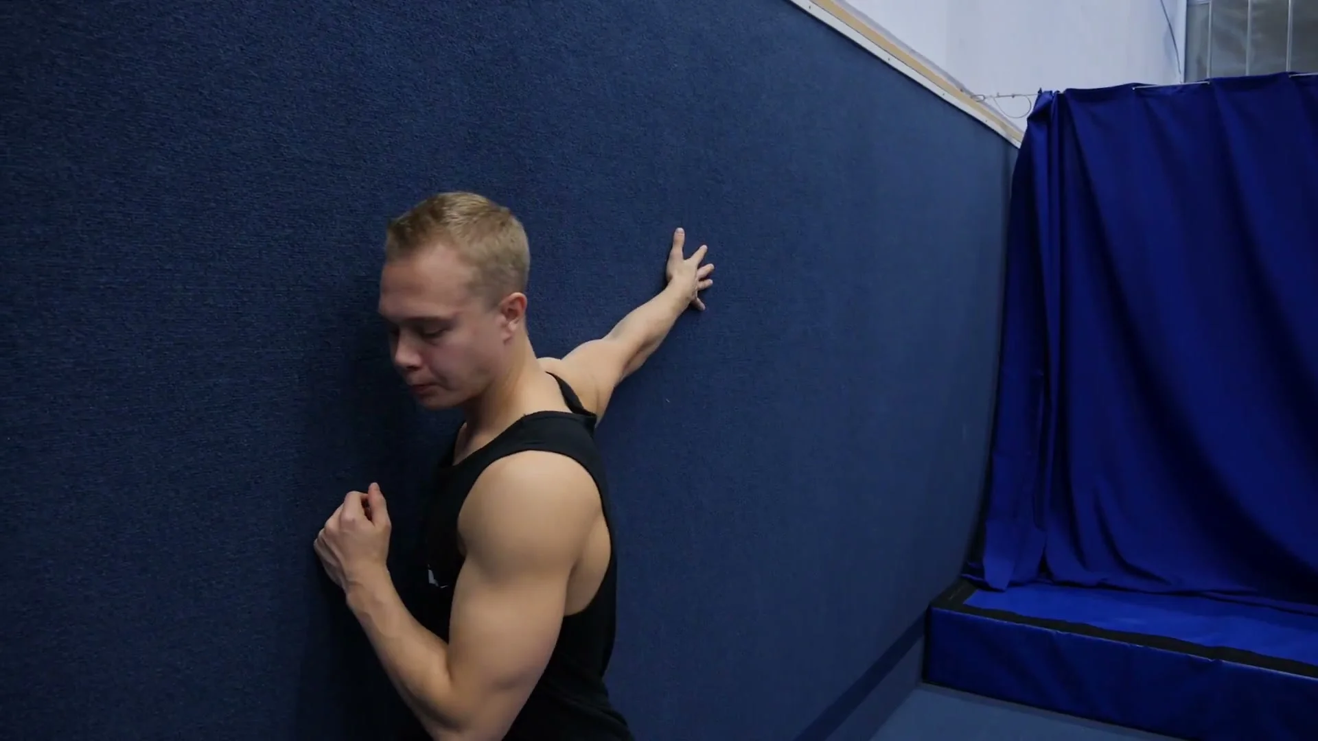 Peg stretch against the wall for hollowback: arm against the wall, body creating stretch through the upper back and shoulder flexion range