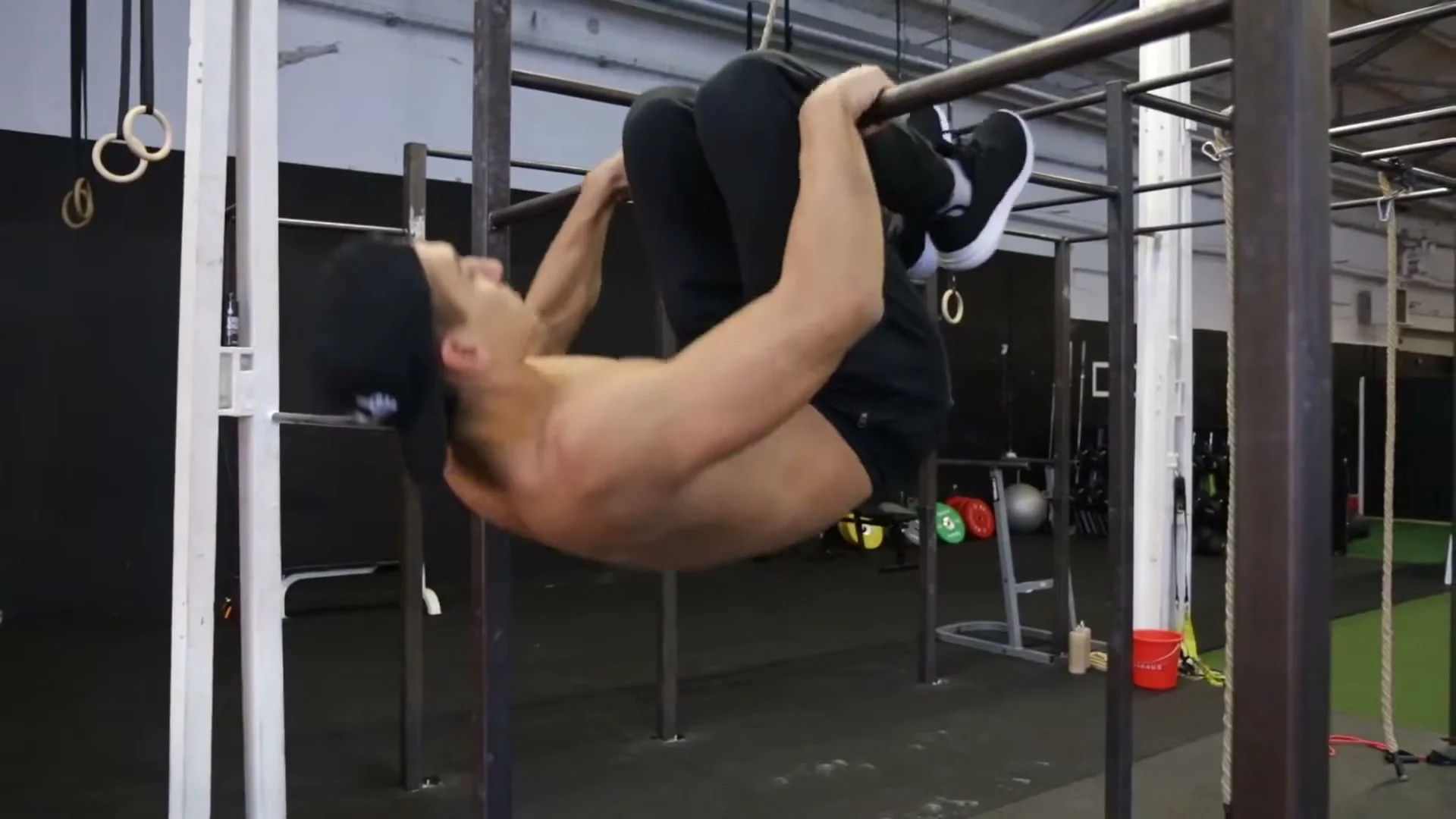 Step 1 of the knee gainer: hanging from a pull-up bar by the knees with the body hanging straight down