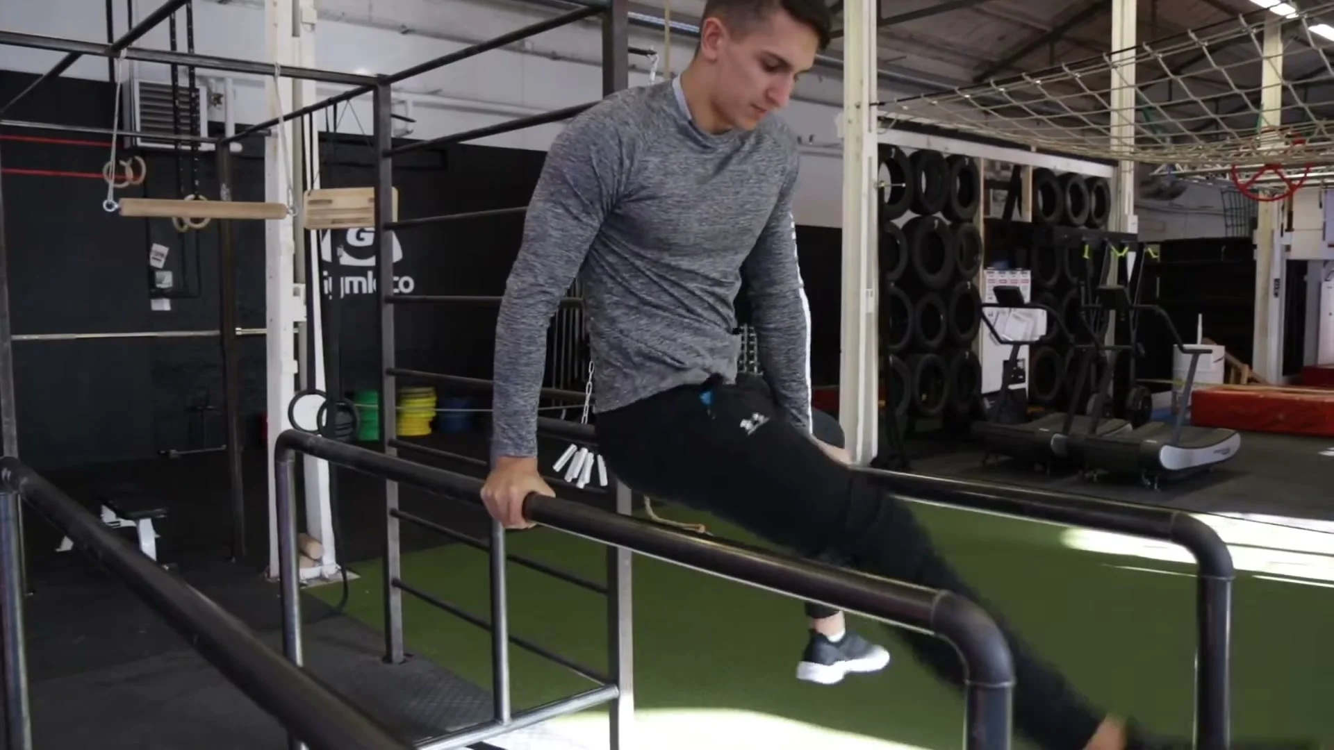 Step 2 of the one leg 360: one foot brought between the bars while one hand moves to the other parallel bar