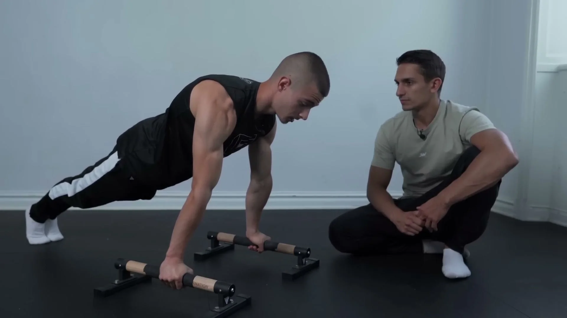 Daniel Hristov performing a push-up on parallettes with Daniel Flefil coaching: straight body line, elbows and biceps facing forward, demonstrating the correct push-up form for planche training